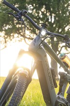 E-bike standing in the green grass with sunlight and trees in the background, quiet and idyllic