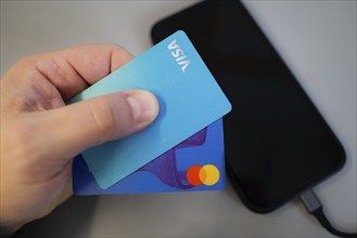 Hand holding two credit cards, for mobile payment, over a black smartphone on a grey background