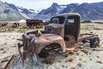 Rusted car and oil drums in front of steep mountains, remains of a US airbase from the Second World