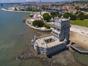 Historic tower on the coast with city in the background and blue water in the foreground, aerial