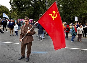 A man wears a Russian uniform and holds a flag of the former Soviet Union during the demonstration