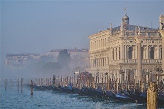 Gondolas lying in the water in front of the doges palace on a foggy morning at sunrise in Venice in