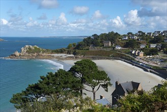 Coastal landscape with sandy beach, surrounded by trees and houses under blue sky, view of sandy