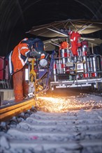 Worker welding a rail in a tunnel with flying sparks and large equipment, rail welding, track