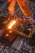 Mechanical device working on rails, surrounded by sparks, protective clothing, rail welding, track