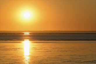 Sunset over the North Sea at low tide, the outline of the island of Juist on the horizon,