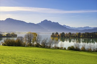 Lake surrounded by meadows and trees in autumn colours with mountains in the background under a