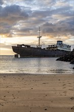 Lost place, ghost ship, A rusty ship lies on the horizon in front of a quiet, sandy beach. The