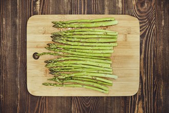 Overhead view of asparagus with seasonings ready for frying on wooden chopping board