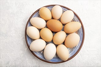 Pile of colored chicken eggs on plate on a gray concrete background. top view, flat lay, close up