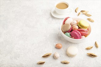 Multicolored macaroons and chocolate eggs in ceramic bowl, cup of coffee on gray concrete