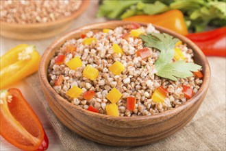 Buckwheat porridge with vegetables in wooden bowl on a white wooden background and linen textile.