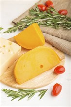 Various types of cheese with rosemary and tomatoes on wooden board on a white wooden background and