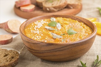 Sweet potato or batata cream soup with sesame seeds in a wooden bowl on a white wooden background