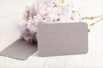 Gray business card with lilac flowers on gray concrete background. side view, copy space, mockup,