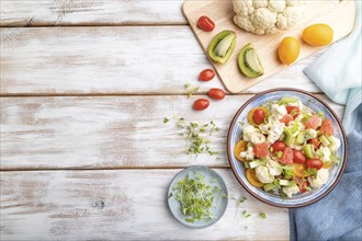 Vegetarian salad of cauliflower cabbage, kiwi, tomatoes, microgreen sprouts on white wooden