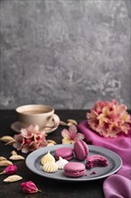 Purple macarons or macaroons cakes with cup of coffee on a black concrete background and pink