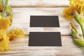 Black business card with iris yellow flowers on white wooden background. side view, copy space,