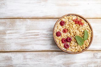 Wheat flakes porridge with milk, raspberry and currant in wooden bowl on white wooden background.