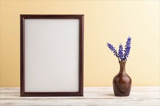 Wooden frame with blue muscari hyacinth flowers in ceramic vase on orange pastel background. side