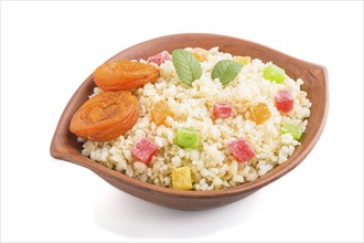 Bulgur porridge with dried apricots and candied fruits in clay bowl isolated on white background.