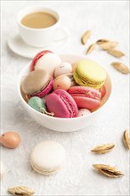 Multicolored macaroons and chocolate eggs in ceramic bowl, cup of coffee on gray concrete