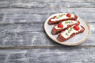 Red beet bread sandwiches with cream cheese and tomatoes on gray wooden background. Side view, copy