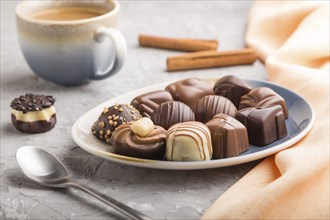 Different chocolate candies and a cup of coffee on a gray concrete background and orange textile.