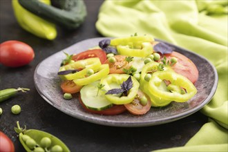 Vegetarian salad from green pea, tomatoes, pepper and basil on a black concrete background and