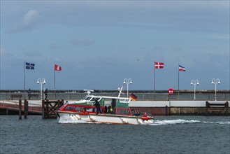 Dune ferry arrives in Heligoland harbour, flags in the wind, pier, offshore island of Heligoland,