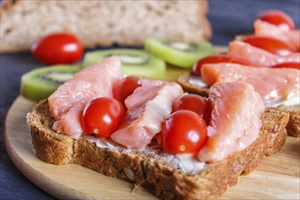 Smoked salmon sandwiches with butter and cherry tomatoes on black wooden background. close up