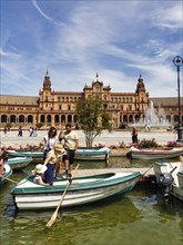 Tourists in rowing boats on a canal, pedestrians on Plaza de Espana, Plaza de España, Seville,