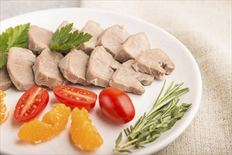 Boiled pork tongue with tomatoes and herbs on a gray concrete background and linen textile. Side