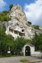 Monastery complex in a rocky landscape with green gate and flag, Bulgarian Orthodox cave monastery,