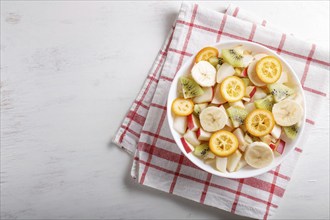 Vegetarian salad of bananas, apples, pears, kumquats and kiwi on linen tablecloth, top view, flat