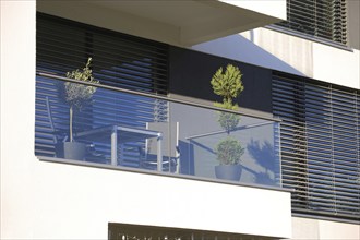 Balcony railing made of glass and stainless steel, behind it windows with modern blinds