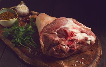 Raw pork knuckle, on a wooden chopping board, with spices, close-up, top view, no people