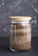 Glass jar with buckwheat poured in layers on a black concrete background. side view, close up.