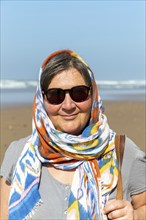 Middle aged woman on beach with sunglasses and head scarf, Morocco, north Africa, Model Released,