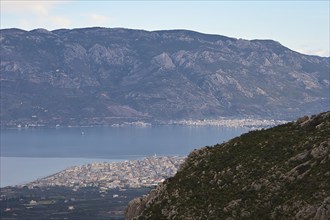 Wide view over a coastal town on the Mediterranean Sea, framed by mountains and clear sky, Archaic