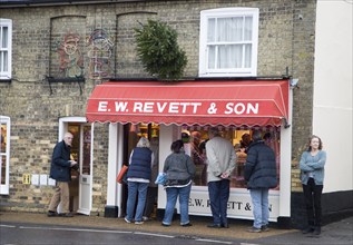 People queue outside E W Revett and Son butcher shop, Wickham Market, Suffolk, England, UK