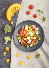 Vegetarian salad with broccoli, tomatoes, feta cheese, and pumpkin on a blue ceramic plate on a