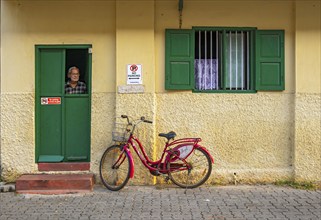 Man looks out a window of yellow house with red bicycle, Fort Kochi, Cochin, Kerala, India, Asia