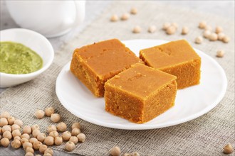 Traditional indian candy burfi in white plate with mint chutney on a gray concrete background. side