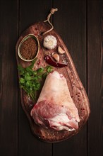 Raw pork knuckle, on a wooden chopping board, with spices, close-up, top view, no people