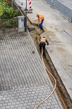 Construction workers lay fibre optic cable in trench under asphalt, cable trench, construction