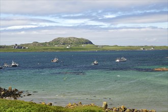 Several boats lying in turquoise blue water, with green hills and an island in the background, view