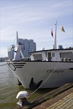 Large ship named Olympia in the harbour in front of modern architecture and bridge, with flags on