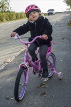 Scared and insecure blonde girl, 3 years old, alone on a bicycle in traffic in Ystad, Skåne County,