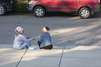 Detroit, Michigan, Two women sit on the curb outside the Shepherd art gallery during its grand